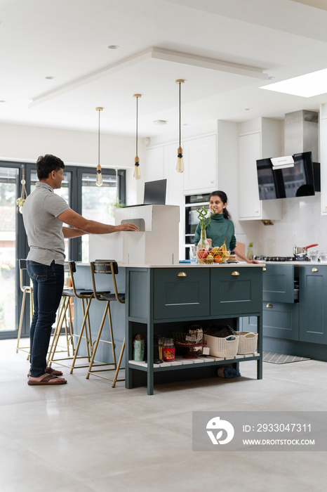 Man talking with wife while working on laptop in kitchen