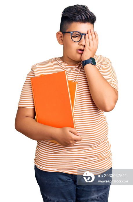 Little boy kid holding book wearing glasses yawning tired covering half face, eye and mouth with hand. face hurts in pain.