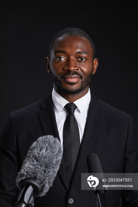 Vertical portrait of confident African-American man standing at podium and giving speech against black background