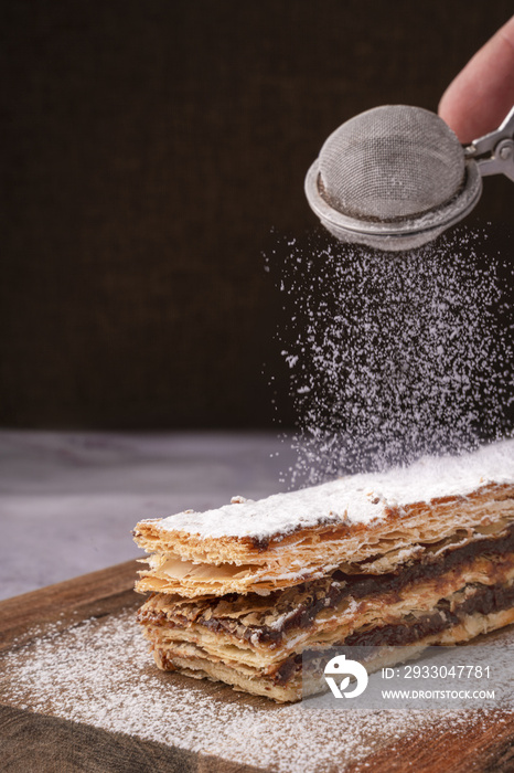 Chocolate millefeuille with sugar falling on it.