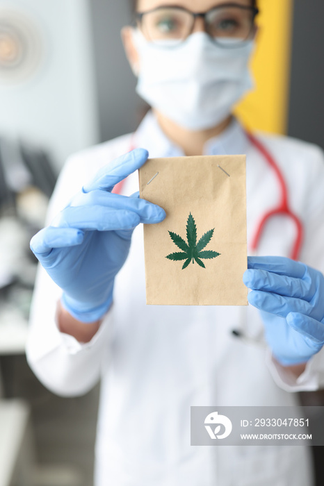 Doctor in rubber gloves holding paper bag with marijuana in clinic closeup. Treatment of cancer with narcotic drugs concept