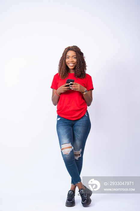 young beautiful black woman using her phone and smiling, standing with legs crossed