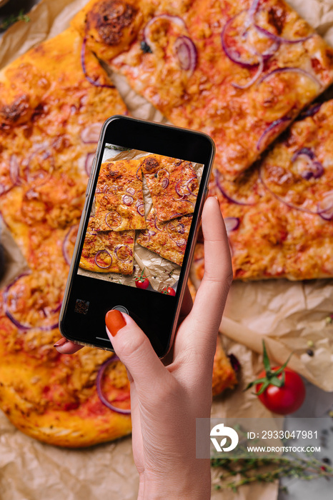 Female hand making a photo of pizza with a mobile phone