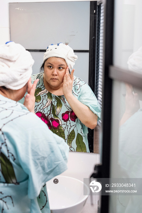 Plus size female examining her skin in the mirror