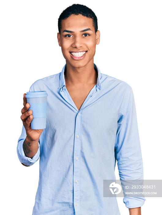 Young hispanic man drinking a take away cup of coffee looking positive and happy standing and smiling with a confident smile showing teeth