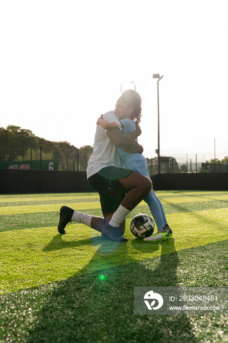 Coach and girl (6-7) hugging on soccer field