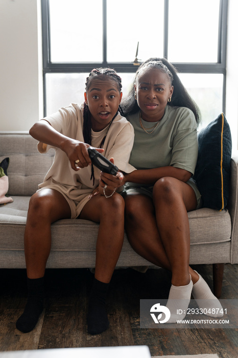 Lesbian couple playing video games while sitting on sofa at home