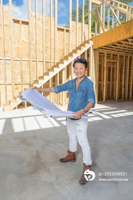 Portrait of mid adult woman holding blueprints to her own home