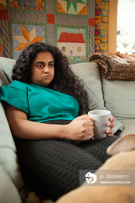 Curvy Indian girl with Cerebral Palsy drinking coffee next to her dog in the living room