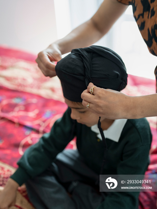 Mother wrapping traditional turban on son’s (6-7) head