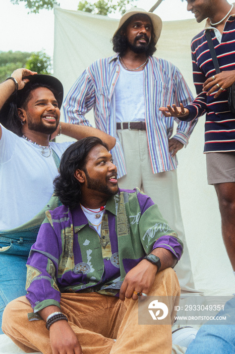 Malaysian Indian men in a group against a cloth backdrop in a park surrounded by trees, talking, laughing and sitting together