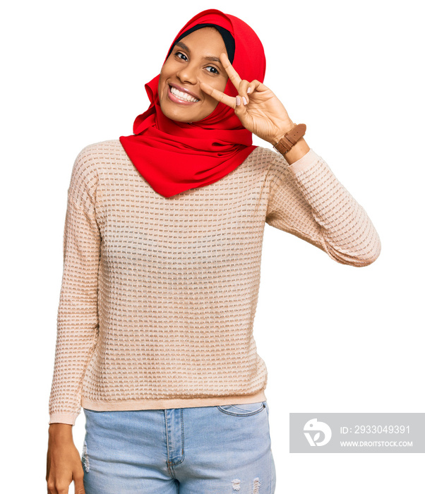 Young african american woman wearing traditional islamic hijab scarf doing peace symbol with fingers over face, smiling cheerful showing victory