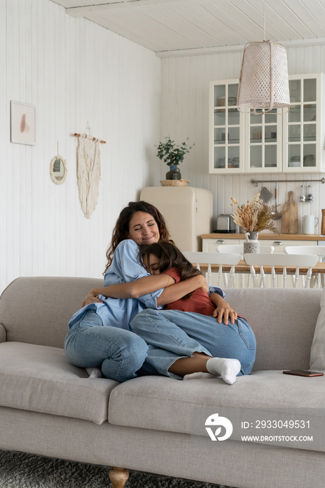 Happy family at home. Loving mother bonding with teenage daughter on weekend, mom hugging embracing teen girl adolescent kid while resting on sofa in living room. Healthy parent-child relationship