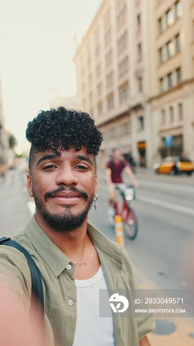 Young happy man with beard, dressed in an olive-colored shirt, stands next to the road, smiles and takes selfie