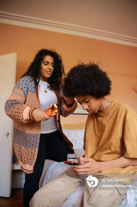 Mid-sized mother helping her son with his hair while he plays on his phone