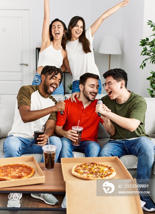 Group of young friends having party eating italian pizza and singing song at home.