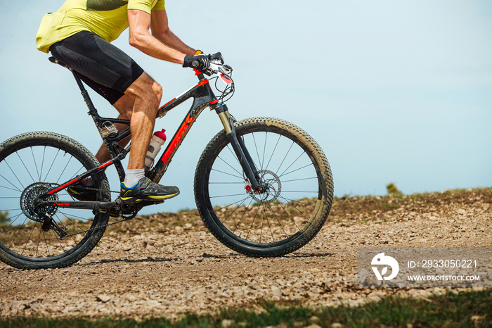 male athlete on mountainbike riding trail on background sky