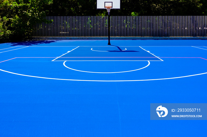 Basketball court in an outdoor park, with intense midday sun, nobody, and blue painted floor.