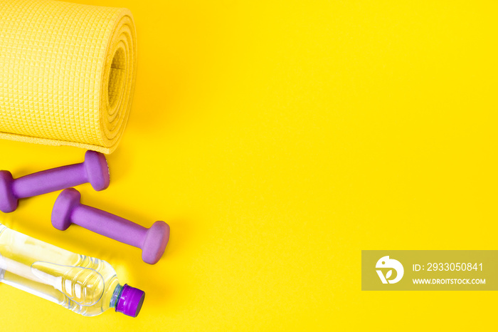 Home fitness concept yellow yoga mat, two purple dumbbells and a bottle of water. Equipment for training and exercises for weight loss. Flat lay a bright background with copy space.