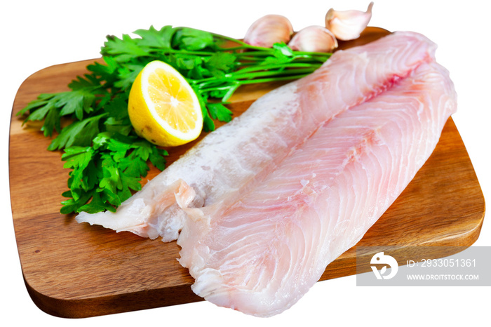 Raw sea perch fillet, garlic, parsley and lemon on wooden cutting board, isolated over white background