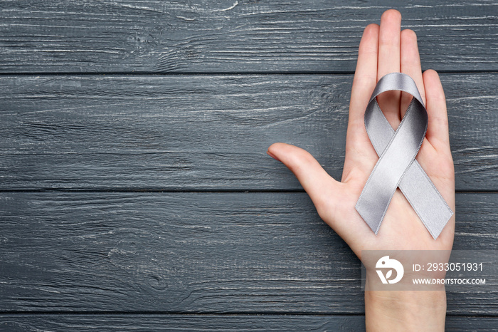 Female hand holding grey ribbon on wooden background. Brain cancer, diabetes, asthma concept