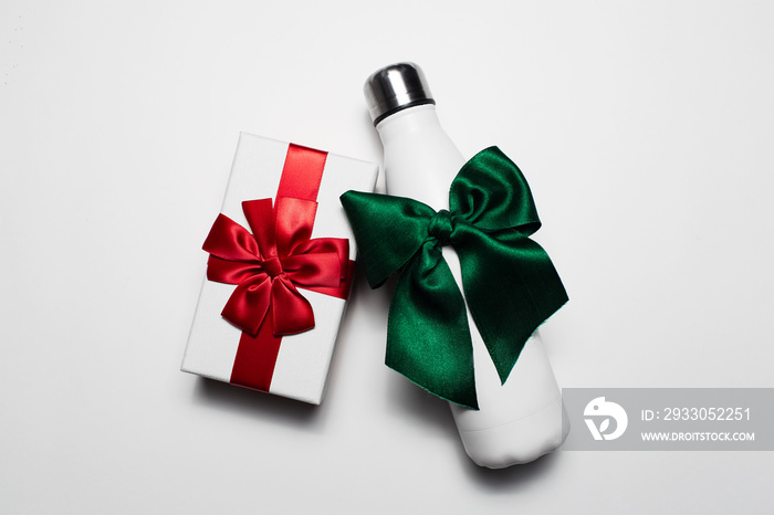 Close-up of gift box and reusable steel thermo water bottle with red and green bows. Isolated on white background.