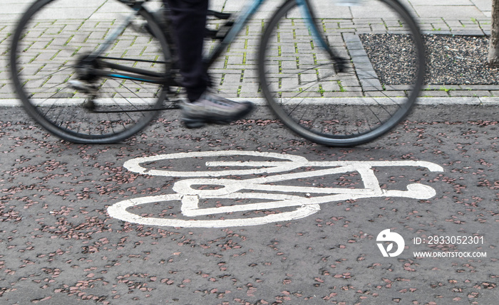 Painted cycle path bicycle sign on the ground with a rider passing.  Motion blurr on the bike and rider.