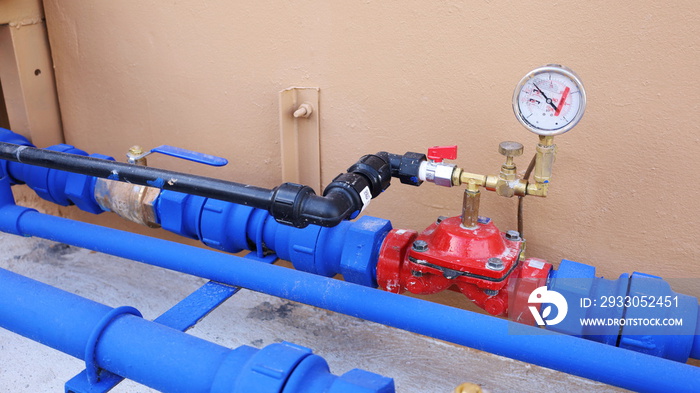 Water pressure reducing valve in the water supply pipe. Red valve with pressure gauge connected between plumbing pipes for high-rise buildings. Focus on the red water valve.