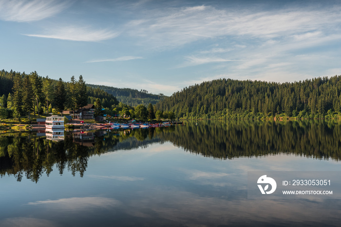 Early morning at Schluchsee in the Black Forest, water reflection, boat rental and shipping pier in background, Baden-Wuerttemberg, Germany