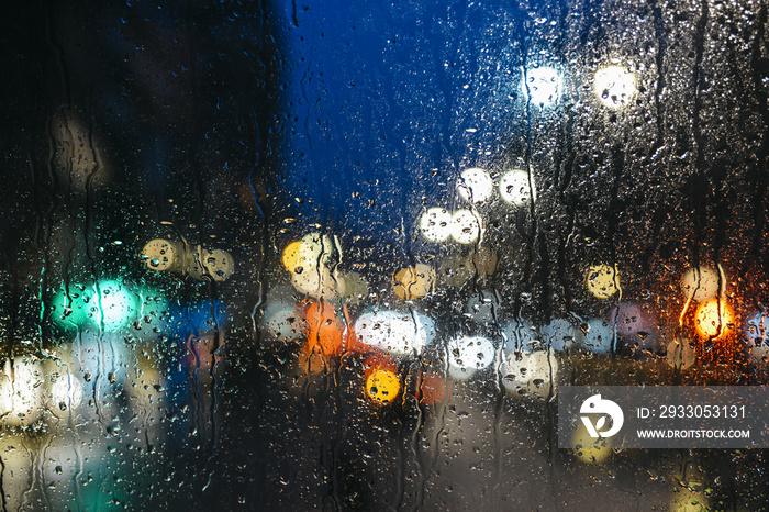 Emotional melancholic abstract background with defocused lights bokeh in London, UK behind rain drops in window glass, Focus on few drops due to the shallow depth of field