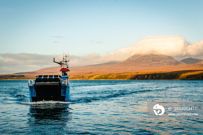 Drifting blue ferry ship between isle of Jura, in the background, and Isle of Skye, in Scotland at sunset time