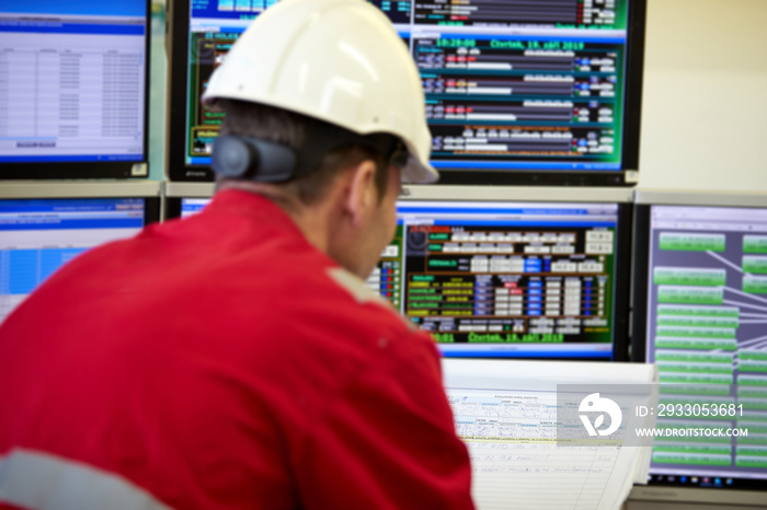 Energy industry. Digital control of heating system. A technician dressed in red overalls and a white helmet checks the heating parameters on the monitors. Supervisory Control And Data Acquisition.