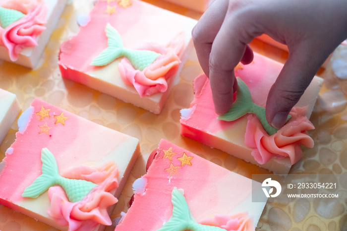 woman using hands to attach mermaid tail to colorful pink green soap making artisanal bath and beauty products as hobby or business