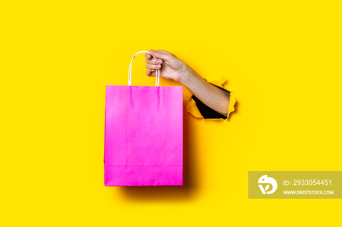 Female hand holds a pink package with purchases on a yellow background