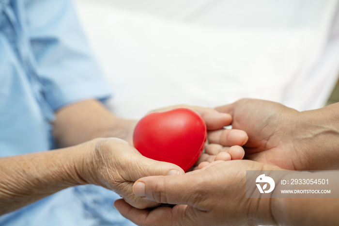 Asian senior or elderly old lady woman patient holding red heart in her hand on bed in nursing hospital ward, healthy strong medical concept