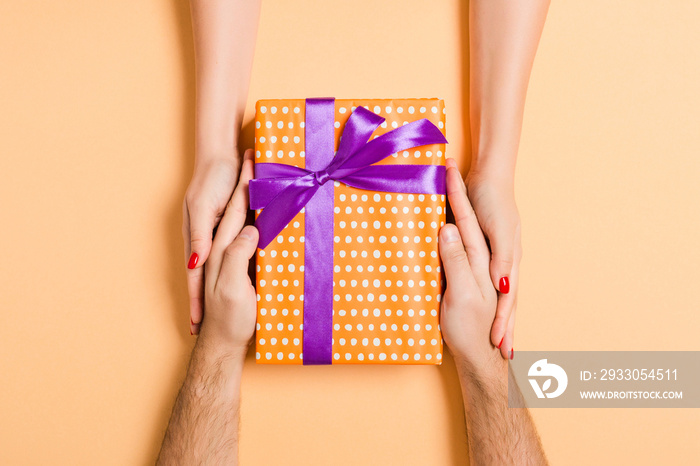 Top view of giving and receiving a gift on colorful background. Present in male and female hands. Love concept. Close up