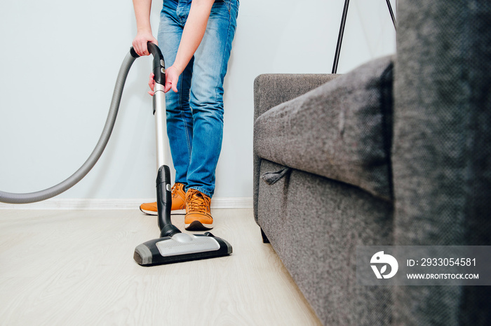 The man is vacuuming in the apartment. A man uses a vacuum cleaner to clean the apartment. Concept of caring for the interior of the apartment, cleaning. Help husbands in housekeeping.