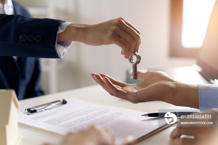 Young Asian couple making contract with house sale agency. Man receiving the house key from female home broker. Close up shot at the house key. Real estate agreement successful concept.