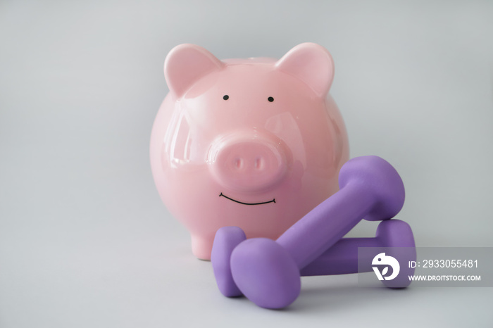 Piggy bank with dumbbells on light background. Weight loss concept