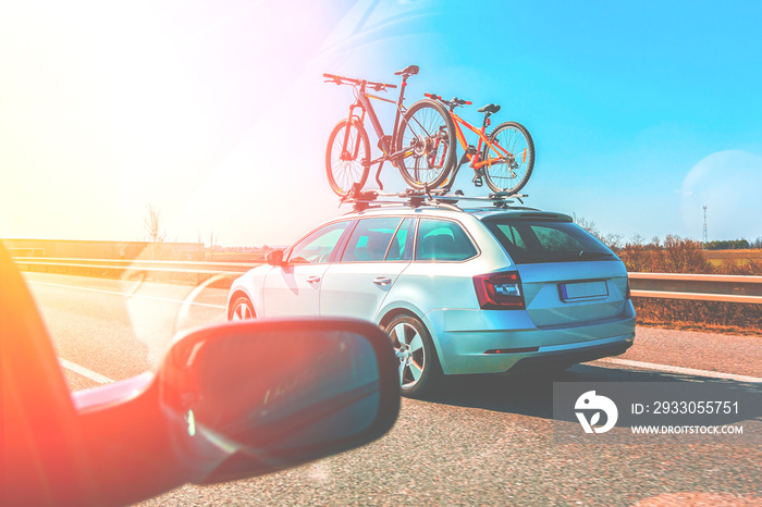 Transportation of mountain bikes on the roof of the car. Bicycle roof mount. Car with two bicycle mounted to the roof on the highway at sunny day.