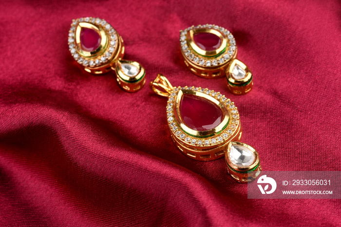 Kundan jewelry placed on red satin with earrings. kundan and red stone pendant,Luxury female jewelry, Indian traditional jewellery, kundan earring,Bridal Gold earrings wedding jewellery