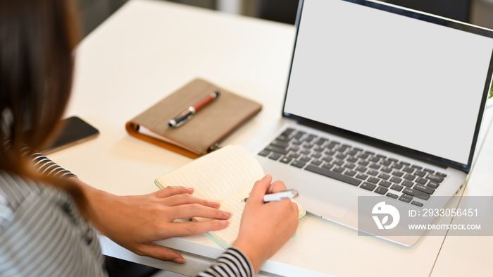 Young businesswoman taking notes in laptop computer, laptop blank screen mockup