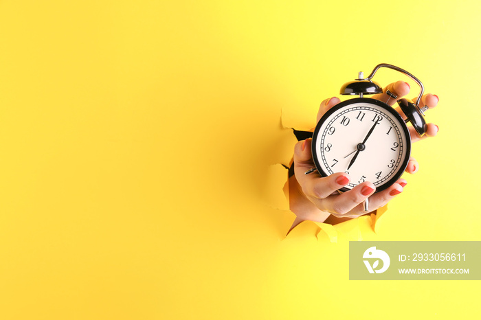 Female hand with alarm clock visible through hole in torn color paper