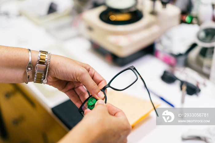 Female optician measuring and preparing glasses on the latest digital device in optical store. Professional ophthalmology instrument in clinic office and optics