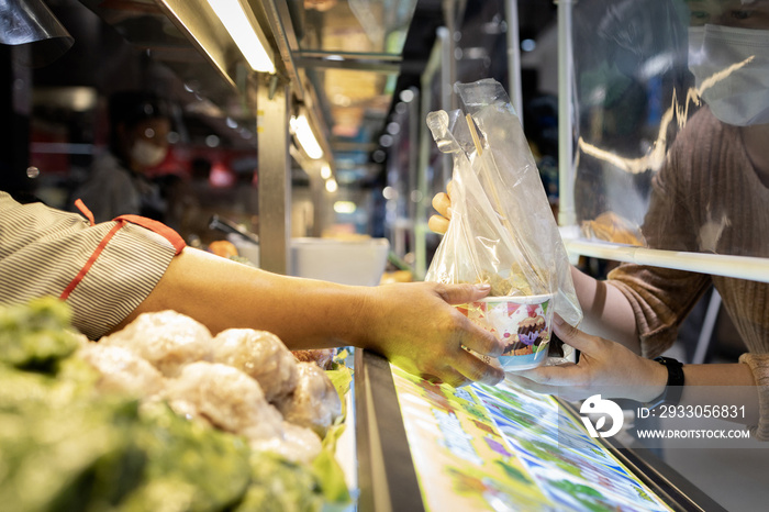 People in a protective mask,buying food in the food court at the mall after Coronavirus quarantine or Covid-19 with plastic shield partition,distancing safety,hygienic,new normal city lifestyle .