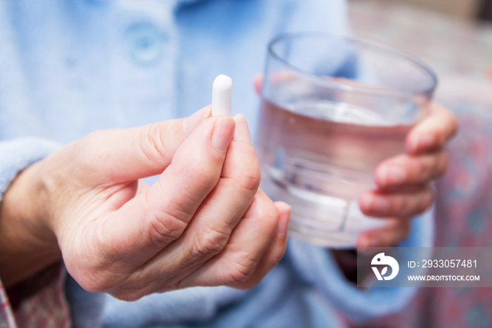 woman with pills or capsules on hand and a glass of water