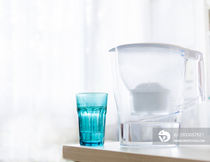 Water filter jug and blue glass with water on light blurred background. Healthy lifestyle. Ecology.