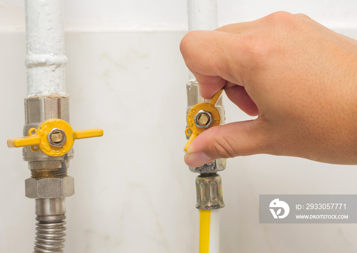 Male’s hand opens yellow handle gas ball valve on gas pipe at home. Part of body, selective focus.