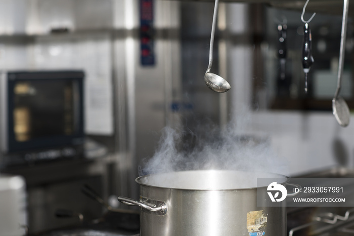 Steam over cooking pot in kitchen on dark background, inox ladle hanging from above the stove