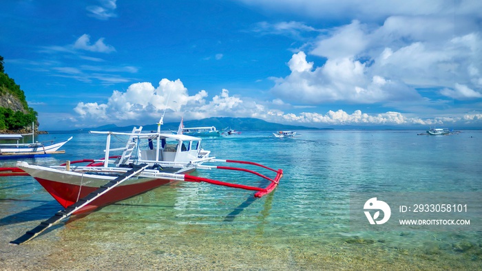 Traditional Filipino wooden outrigger boats, locally known as a banca, in the shallow turquoise water of Puerto Galera, a resort town on Mindoro Island, Philippines.